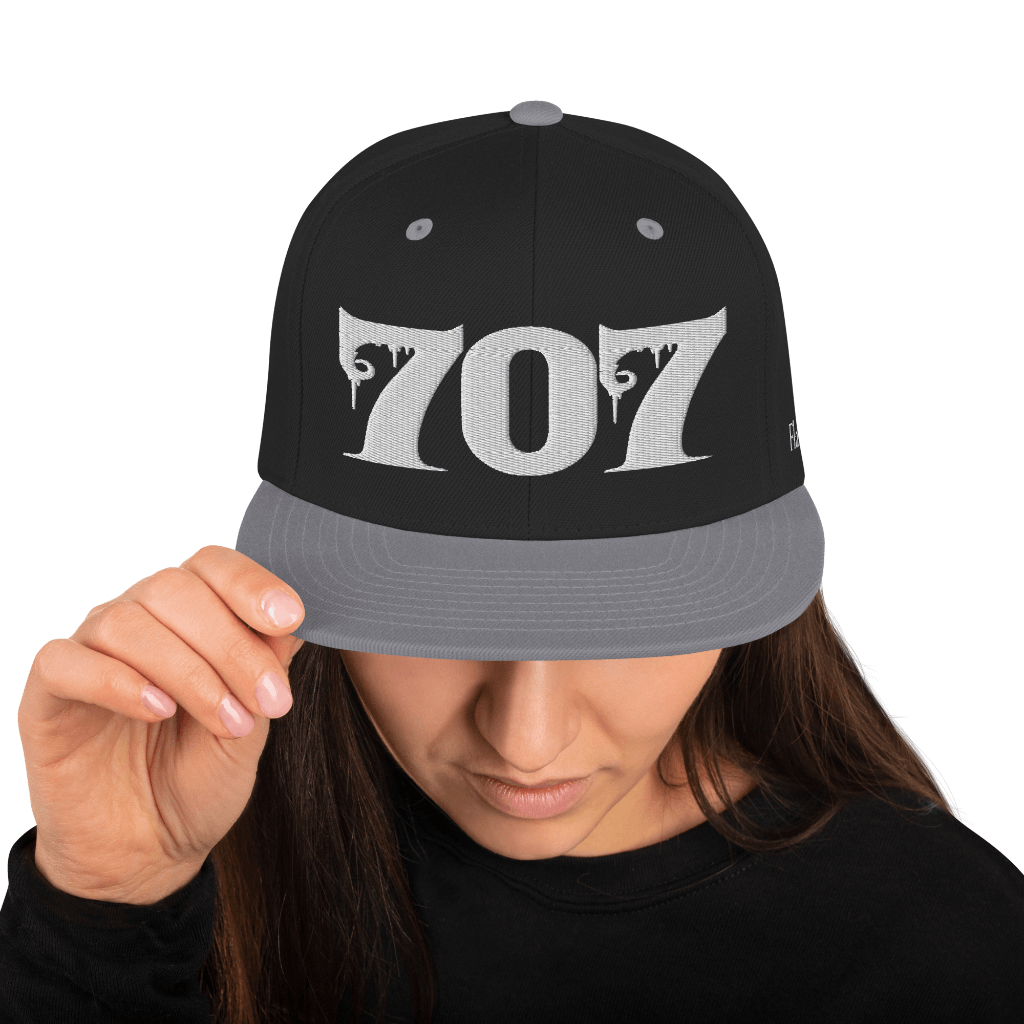 Woman wearing Deadpan Couture 707 Classic Snapback Hat in black with white gothic-style '707' embroidery.