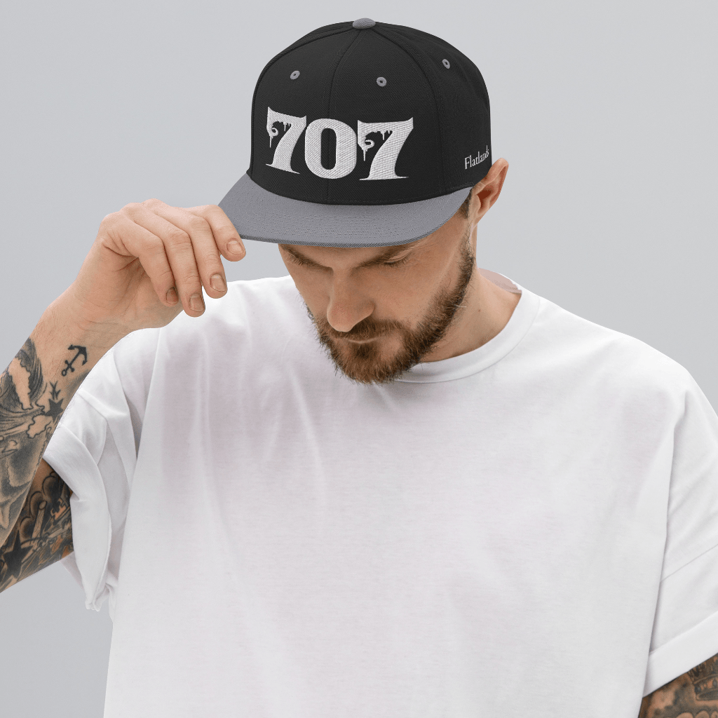 Man wearing Deadpan Couture 707 Classic Snapback Hat in black with white gothic-style '707' embroidery.