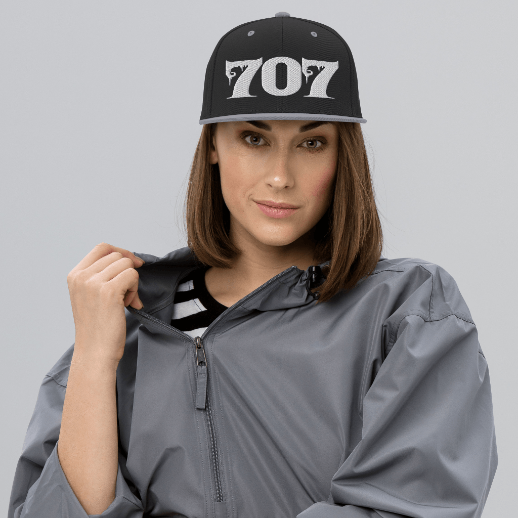 Woman wearing Deadpan Couture 707 Classic Snapback Hat in black with white gothic-style '707' embroidery.