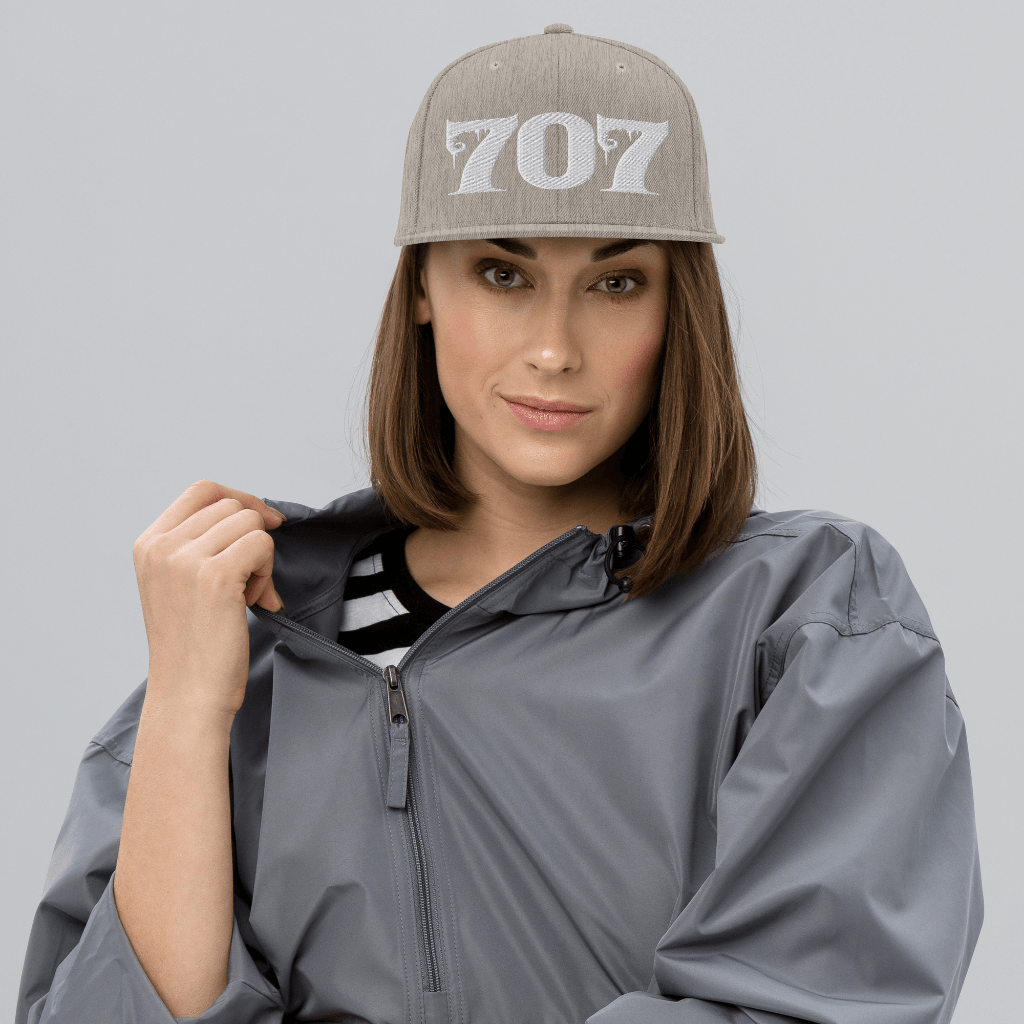 Woman wearing Deadpan Couture 707 Classic Snapback Hat in black with white gothic-style '707' embroidery.