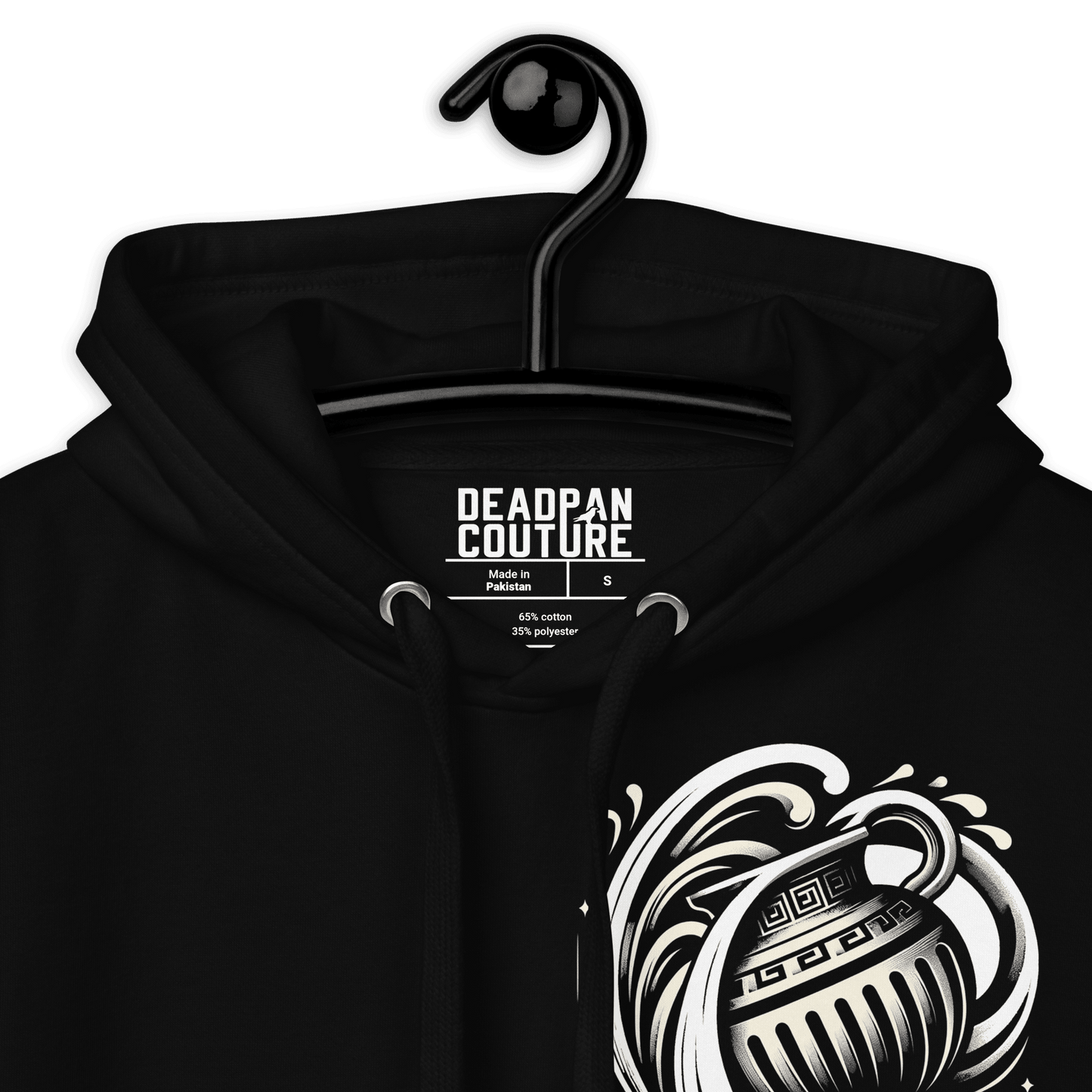 A close-up view of a black hoodie on a hanger, showcasing the intricate details of a stylized silver Aquarius water-bearer symbol on the left chest. The Deadpan Couture label is prominently displayed inside the hoodie, with text indicating that it is made in Pakistan and composed of 65% cotton and 35% polyester. The hoodie's drawstrings and eyelets are also visible in the image, emphasizing the garment's quality craftsmanship.