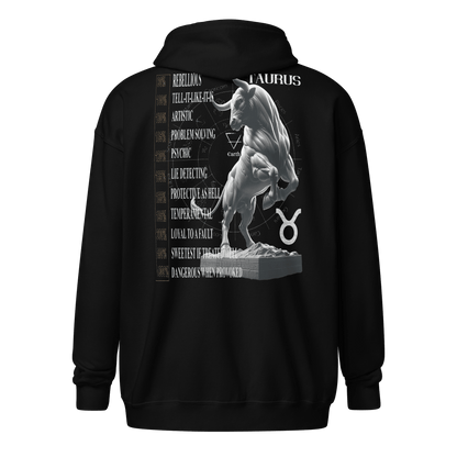 A black unisex heavy blend zip hoodie with a bold graphic on the back. The design features a powerful, detailed Taurus bull standing on a pedestal. Surrounding the bull are keywords describing Taurus traits such as "Rebellious," "Artistic," "Protective as Hell," and "Dangerous When Provoked." The Taurus symbol and the word "Taurus" are also prominently displayed.