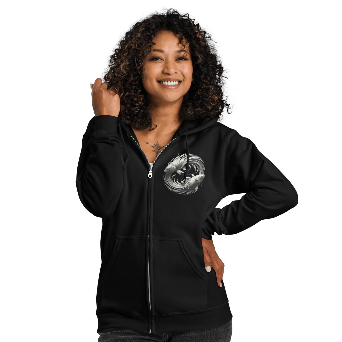 A woman with curly hair is smiling while wearing the black Deadpan Couture zip-up hoodie. The front of the hoodie showcases a small, detailed graphic on the left chest area featuring two stylized fish swimming in a circular motion, symbolizing the Pisces zodiac sign. The casual, comfortable style is highlighted by the full-zip design.