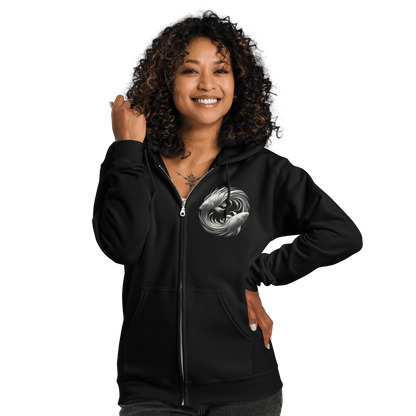 A woman with curly hair is smiling while wearing the black Deadpan Couture zip-up hoodie. The front of the hoodie showcases a small, detailed graphic on the left chest area featuring two stylized fish swimming in a circular motion, symbolizing the Pisces zodiac sign. The casual, comfortable style is highlighted by the full-zip design.