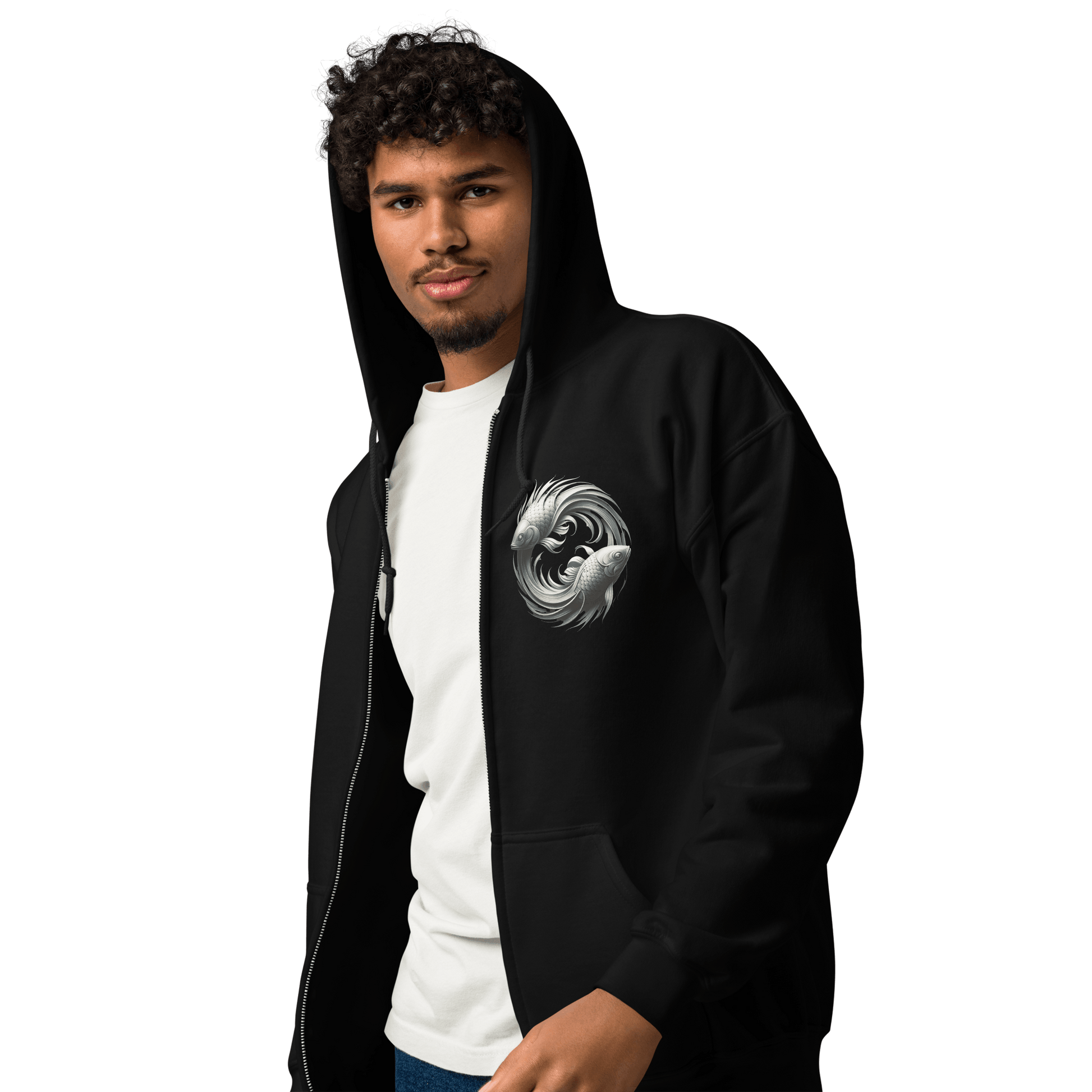 A man with curly hair is wearing a black Deadpan Couture zip-up hoodie. The front of the hoodie features a small, detailed design on the left chest area, depicting two stylized fish swimming in a circular motion, representing the Pisces zodiac sign. The man pairs the hoodie with a white t-shirt underneath, exuding a casual and stylish look.