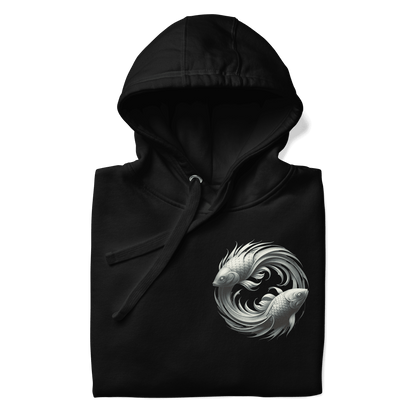 A folded black Deadpan Couture hoodie showcasing the left chest area design. The front features a small, intricate graphic of two stylized fish swimming in a circular pattern, representing the Pisces zodiac sign. The monochrome design is detailed and stands out against the dark fabric.