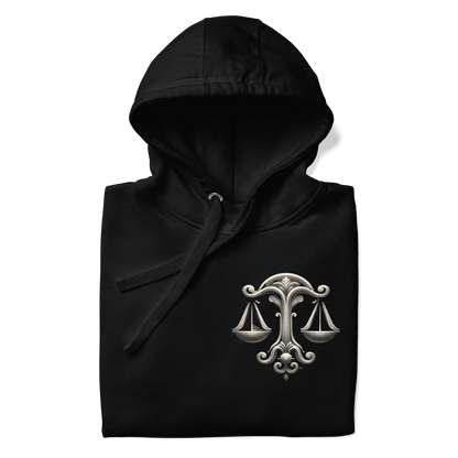 A neatly folded black Deadpan Couture hoodie showcasing the detailed design on the left chest area. The graphic features an ornate set of scales, symbolizing the Libra zodiac sign. The intricate design contrasts beautifully with the black fabric, making the hoodie visually appealing even when folded.