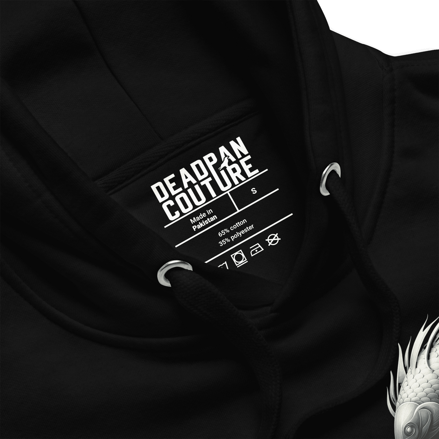 A close-up view of the inside of the Deadpan Couture hoodie, focusing on the label. The label indicates the brand name, sizing, and fabric composition (65% cotton, 35% polyester). The image also includes a portion of the Pisces graphic on the left chest, adding a subtle touch of the design.