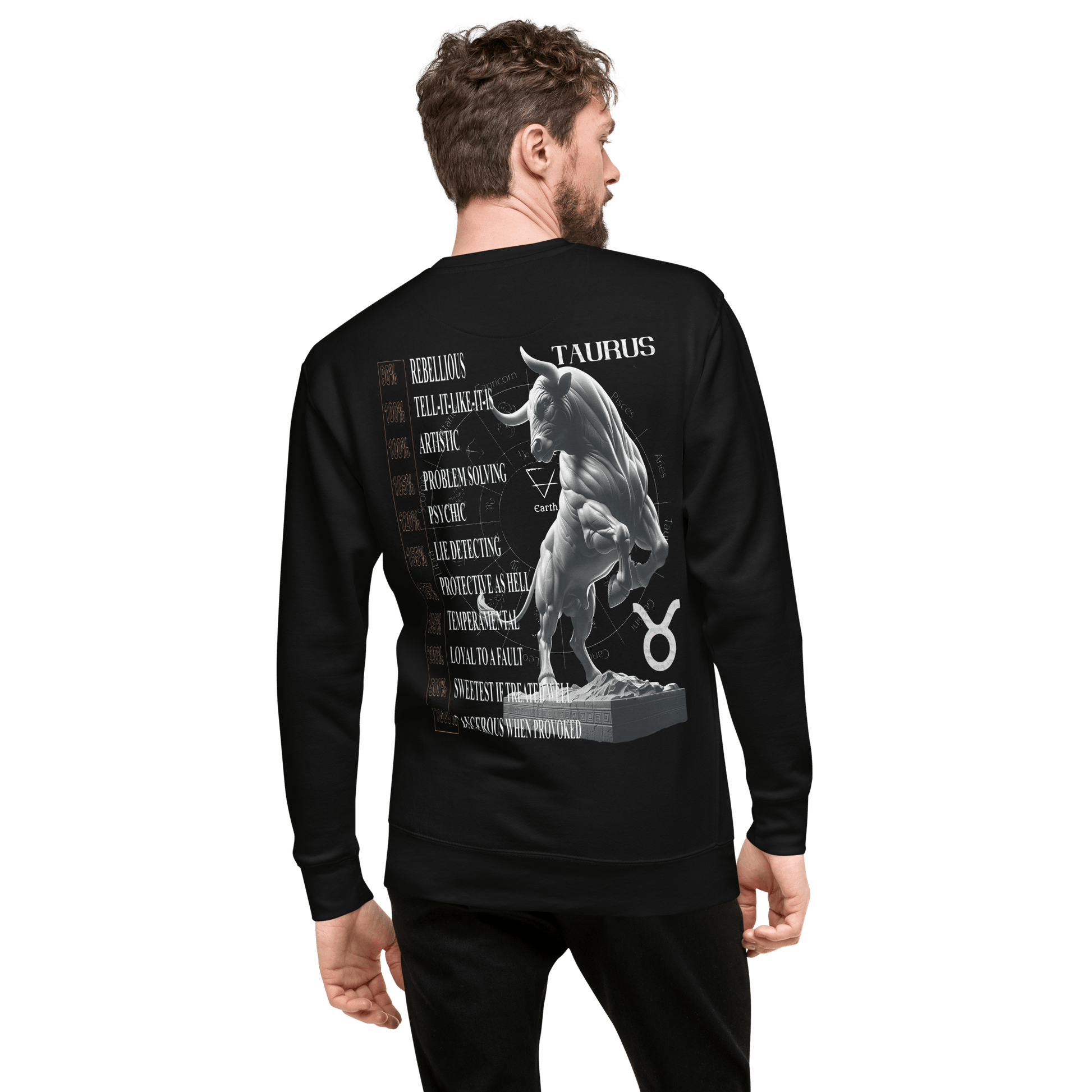 A man with short hair, viewed from the back, is wearing a black Deadpan Couture sweatshirt. The back features a detailed illustration of a muscular Taurus bull statue. Alongside the statue are various attributes of the Taurus sign listed vertically, such as rebellious, artistic, and loyal.